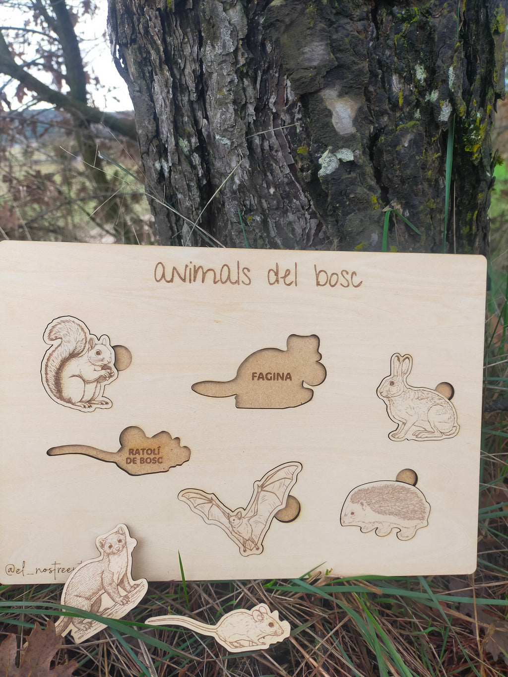 Wooden board with laser-cut animal shapes and text 'animals del bosc' against a natural background.